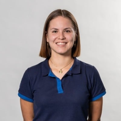 Smiling woman with shoulder-length brown hair wearing a navy blue polo shirt with blue trim against a white background